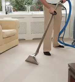 Professional carpet cleaner using a hot-water extraction wand and hose machine in a living room in Philadelphia, PA.