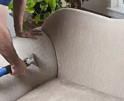 Professional upholstery cleaner deep-cleaning a fabric sofa with a handheld extraction tool and hose in Philadelphia, PA.